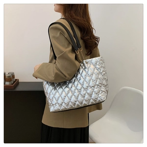 Detail view of quilted silver tote bag with gold chain links and black straps