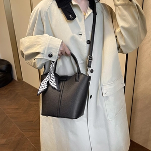 Black lychee leather bucket bag with silk scarf on handle worn with beige coat