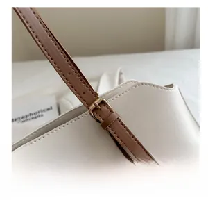 Gros plan sur la boucle métallique réglable et les coutures du sac en cuir beige et brun
