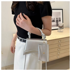 Gros plan d'un sac à main sablier argenté avec poignée nouée et mini breloque pochette