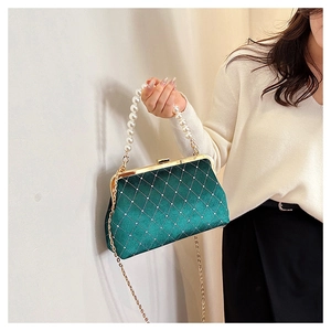 Close-up of green velvet evening bag with quilted texture, pearl handle and gold chain