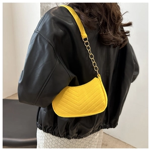 Detail of yellow V-quilted baguette bag with gold chain strap on black leather jacket