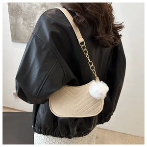 Detail of beige quilted shoulder bag with gold chain strap and white pompom accessory