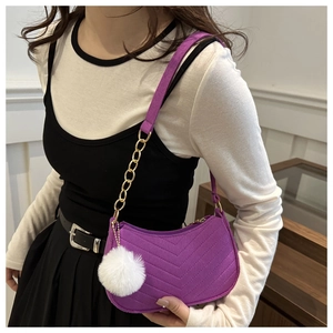 Detail of purple chevron quilted shoulder bag with white pompom charm on a metal chain