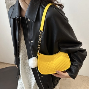 Borsa a spalla gialla a mezzaluna con motivo a V, catena dorata e ciondolo a pompon