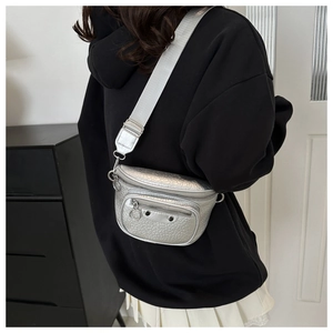 Detail of silver metallic waist bag featuring black studs and wide fabric strap