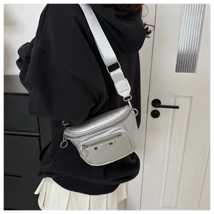 Detail of silver crocodile-textured crossbody bag with wide strap on a female model