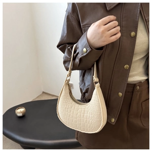 Detail of a creamy white crescent underarm bag with crocodile embossed leather pattern