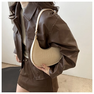 Side view of beige crescent underarm bag with crocodile texture on a model