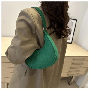 Side view of a green crocodile embossed crescent underarm bag with metal accents