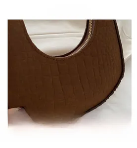 Detail showing the brown crocodile texture and golden zipper on the crescent bag