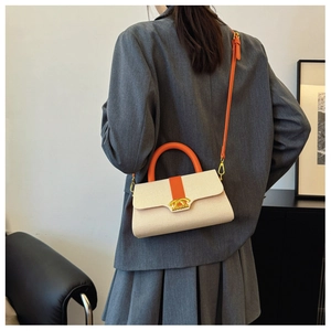 Detail der cremefarbenen Webhandtasche mit orangefarbenem Ledergriff auf grauem Blazer