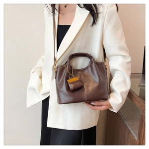 Detail of a brown leather tote bag with vertical stitching and gold chain charm