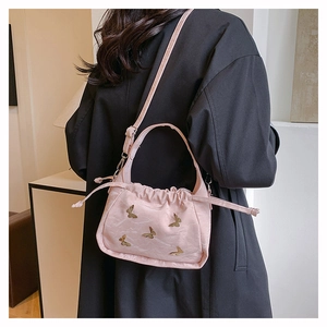 Sac seau rose avec détails de papillons dorés porté sur un manteau noir élégant