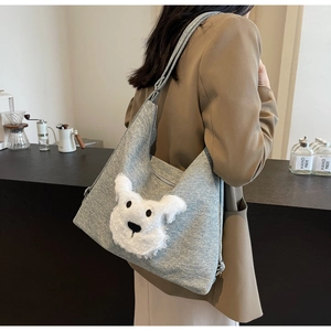 Close-up of a plush puppy tote bag on a brown blazer model in a cozy cafe setting