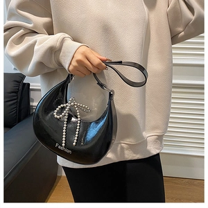 Detail of black glossy leather crescent bag featuring a pearl bow charm and logo