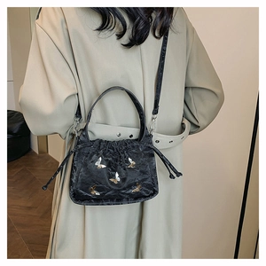 Sac à bandoulière noir à cordon avec motifs papillon porté sur un trench-coat classique
