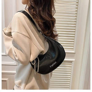 Detail of a black glossy hobo bag with Fashion text and a gold beaded chain accessory