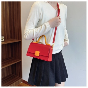 Detail of red luxury crossbody bag featuring yellow handle and floral buckle decoration