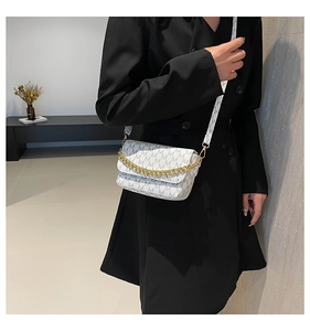 Close-up of white shoulder bag with M pattern, gold chain and wide crossbody strap