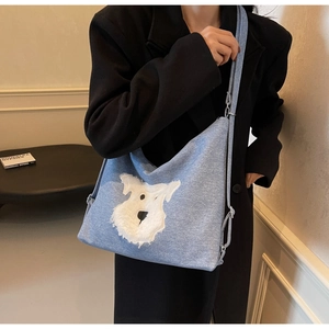 Detail of light blue denim crossbody bag with white plush dog motif on black coat