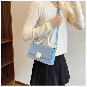 Detail of light blue crossbody bag featuring a white flower clasp and wavy handle