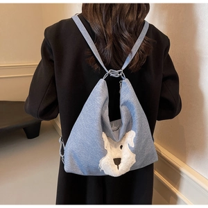 Détail d'un sac en denim bleu clair avec un écusson de chiot en peluche blanche et sangle