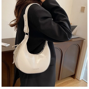 Detail of white glossy crescent bag with hanging pearl charms and adjustable strap