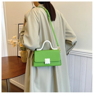 Detail of green crossbody bag with wavy white handle and floral petal clasp