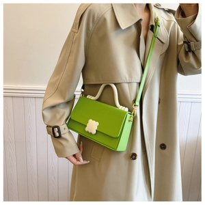Detail of green leather handbag with white U-shaped handle and floral clasp worn on trench coat