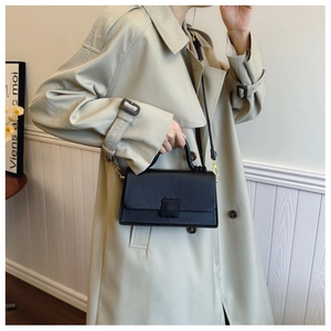 Close-up of black leather crossbody bag with flower-shaped buckle on a beige trench coat
