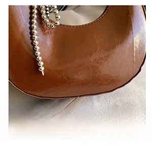 Detail of brown pleated faux leather hobo bag with silver ball chain and logo