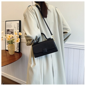 Structured black leather handbag with petal clasp shown on model in minimalist interior