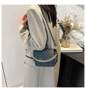 Detail of grey crossbody bag with gold chain and M letter patterns on a grey suit