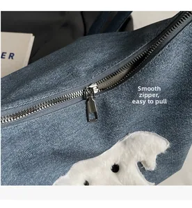 Detail of blue denim bag featuring a smooth silver zipper and white plush puppy patch