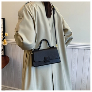 Detail of black crossbody bag with floral buckle, styled with a beige trench coat
