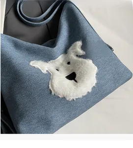 Detail of blue denim tote bag with cute white plush puppy patch and black handles