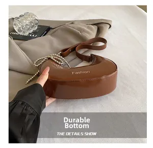 Detail of a brown glossy leather crescent bag featuring a silver bead decorative chain