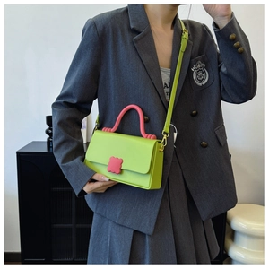 Detail of neon green crossbody bag with pink contrast handle worn on a grey blazer