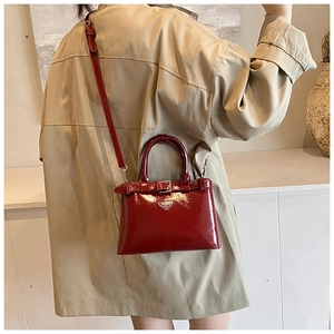 Mannequin portant un sac bandoulière rouge en cuir verni avec plaque argentée