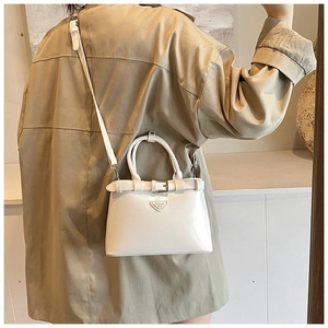 Détail d'un petit sac blanc brillant avec boucle en métal porté sur un trench-coat