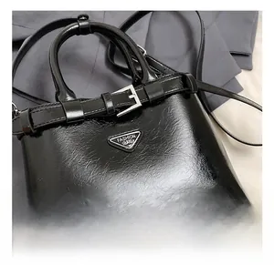 Gros plan du sac en cuir brillant noir avec logo métallique argenté et boucle