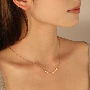 Détail du collier doré avec pendentif sourire incurvé et petits motifs de cœurs