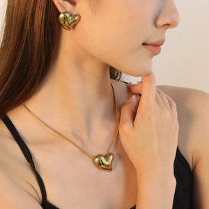 Close-up of model wearing chunky golden heart pendant necklace and matching stud earrings