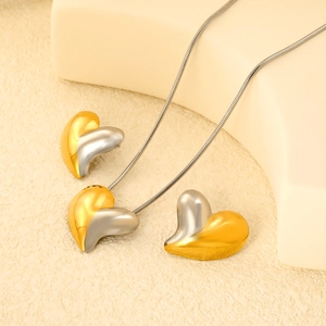 Detail of two-tone heart necklace and earrings set on a minimalist display stand
