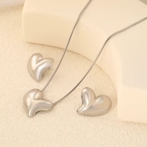 Polished silver heart pendant necklace and stud earrings set on minimalist display