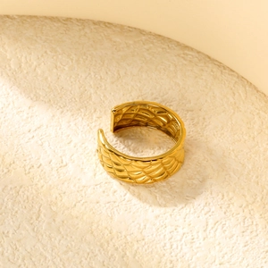 Close-up of golden adjustable ring with quilted motif texture on a stone background