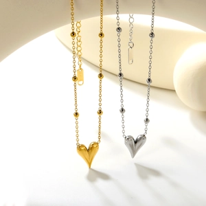 Dettaglio di collane a cuore oro e argento con catene a perline su basi minimaliste