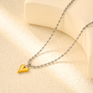 Dettaglio di un ciondolo a cuore dorato con catena a sfere argentata su sabbia beige