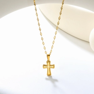Detail of a vintage golden cross pendant with milgrain edges on a minimalist ceramic base